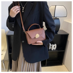 Close-up of brown leather crossbody bag with gold metal buckle on a black blazer