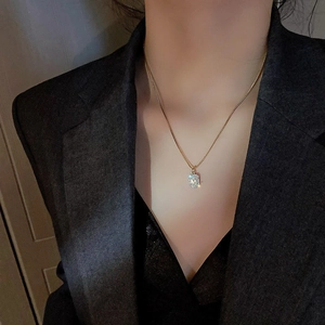 Close-up of golden letter M necklace with micro-pave zircons worn on a dark suit