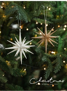 Glittery white and gold star ornaments hanging on a Christmas tree with bokeh lights