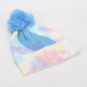 Close-up of tie-dye knit beanie featuring a large blue faux fur pompom and rolled cuff