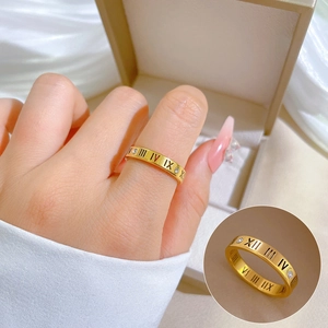 Minimalist gold Roman numeral ring with white crystals on a warm beige background