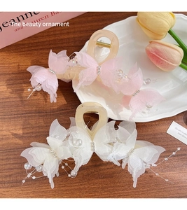 Detail of resin butterfly hair claw with organza wings, pearls, and tassel on wood background