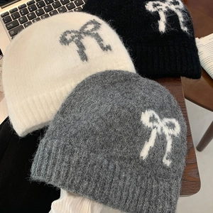 Flat lay of knit beanies in ivory, black, and grey featuring stylish bow patterns