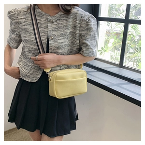 Close-up of yellow pebbled leather crossbody bag with striped strap and silver zipper