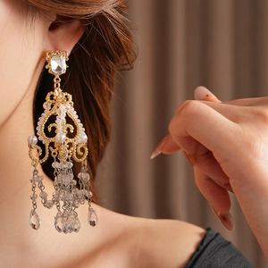 Close-up of golden chandelier drop earrings with glass tassels and pearls on a model