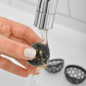 Sticky reusable purse cleaning ball being rinsed under water to remove dust and debris