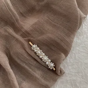 Detail of baroque pearl hair clip with gold alloy finish on textured fabric backdrop