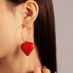 Detail of red acrylic heart pendant on golden hoop earring worn by a model