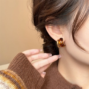 Close-up of amber resin and gold metal geometric earrings worn by a model in warm light