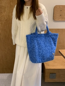 Dettaglio di una borsa tote blu in peluche con ciondolo a cuore indossata con un maglione