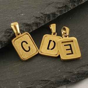 Macro shot of gold rectangle letter pendants with frosted texture on dark stone surface