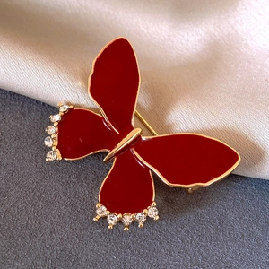 Macro detail of a red enamel bow brooch with gold edges and white sparkling rhinestones