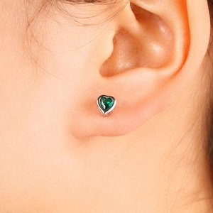 Detail of silver heart stud earrings featuring a claw-set green gemstone on ear