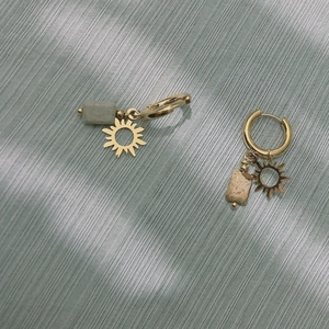 Détail de boucles d'oreilles soleil dorées avec pierre naturelle sur tissu gris