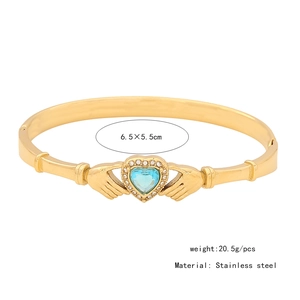 Macro detail of a golden Claddagh bracelet with light blue heart gemstone and 6.5x5.5cm size