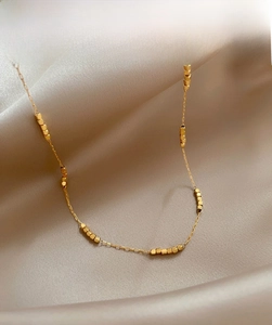 Detail of gold beaded geometric necklace on champagne velvet background showcasing texture