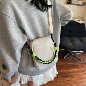 Close-up of off-white canvas crossbody bag with decorative braided rope and plastic buckle