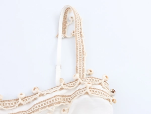 Detailed close-up of white bohemian top with beige woven lace and decorative beads