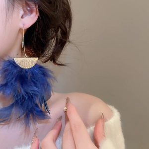 Detail of long bohemian earrings with gold hammered metal and deep blue feathers