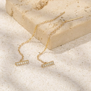 Close-up of gold chain earrings with rectangular diamond accents on stone background