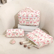 Three-piece quilted cotton makeup bags with pink bow and rose pattern on a beige sofa
