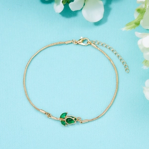 Elegant gold tulip bracelet with green crystals on blue fabric background for women