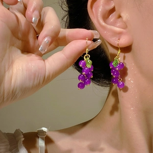 Close-up of handmade purple grape earrings with green leaves worn by a model
