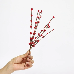 Close-up of vibrant red artificial Christmas berry stems held against a plain white background