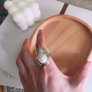Detailed view of baroque pearl ring with golden wavy metal frame on wood tray