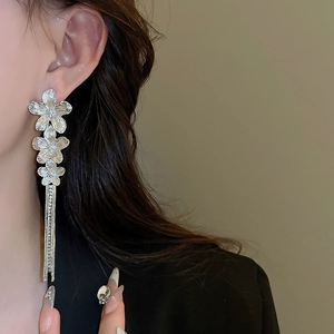 Detail view of silver floral earrings with long tassels on a model's ear