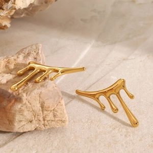 Nahaufnahme goldener Ohrringe im Liquid-Drip-Design auf strukturiertem Naturstein