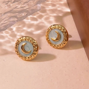 Detail view of retro gold crescent moon earrings with light blue enamel on warm background