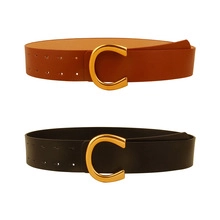 Detail of wide black and tan leather belts with large golden C-shaped buckle