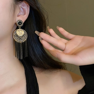 Détail de boucles d'oreilles vintage dorées avec pompons noirs portées par un mannequin