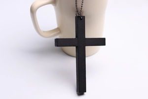 Close-up of black wooden cross pendant with silver bead chain on beige ceramic mug