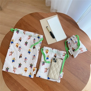 Three-piece set of cotton drawstring bags with bear prints and green cords on a desk