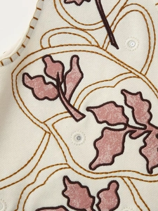 Macro detail of floral embroidery and mirror sequins on a white sleeveless vest