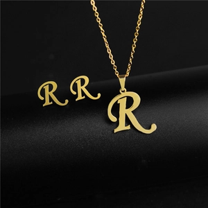Detail of gold letter R pendant necklace and matching stud earrings on black surface