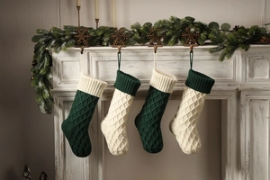 Grüne und cremeweiße gestrickte Weihnachtssocken an einem festlich verzierten Kamin