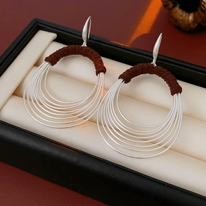 Close-up of silver multilayer oval hoop earrings with brown cord detail in a jewelry box
