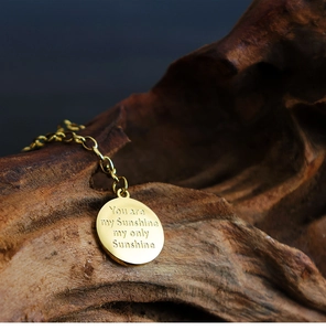 Close-up of golden sunflower pendant with engraved You are my Sunshine quote