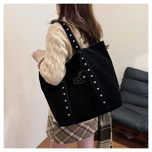 Detail view of large black suede tote bag with metal studs and heart-shaped charm