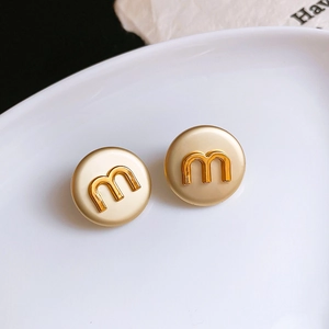 Detailed macro view of minimalist round stud earrings with golden letter m engraving