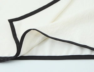 Close-up of white crepe fabric with contrast black trim and detailed woven texture