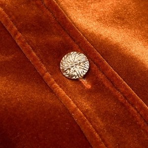 Detailed close-up of caramel velvet fabric and a golden textured button on a jacket