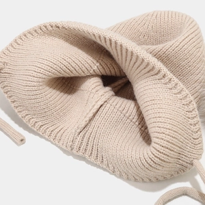 Détail du bonnet en tricot beige montrant la texture côtelée et les liens assortis