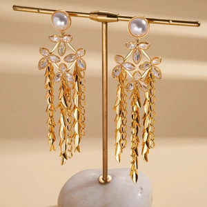 Macro detail of 18K gold plated tassel earrings with pearl studs and leaf chains