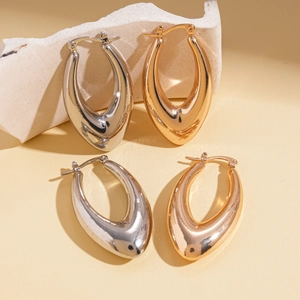 Polished gold and silver teardrop hoop earrings displayed on a minimalist stone base