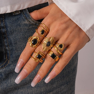 Détail de bagues dorées superposées avec pierres noires sur une main sur denim