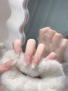 Macro detail of French tip press-on nails with white pearls and gold beads on pink base